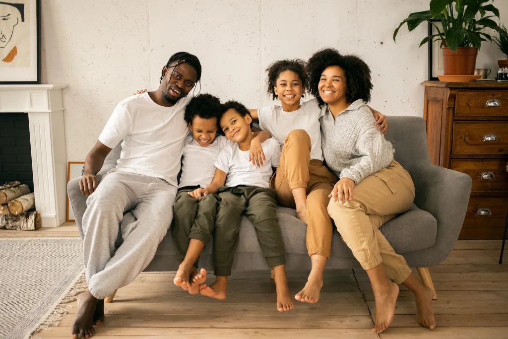 89 TINY HOME STATISTICS & FACTS: EXPLORE TINY HOME MARKET TRENDS 8 Full body of cheerful African American parents with children looking at camera while sitting on sofa in room with fireplace