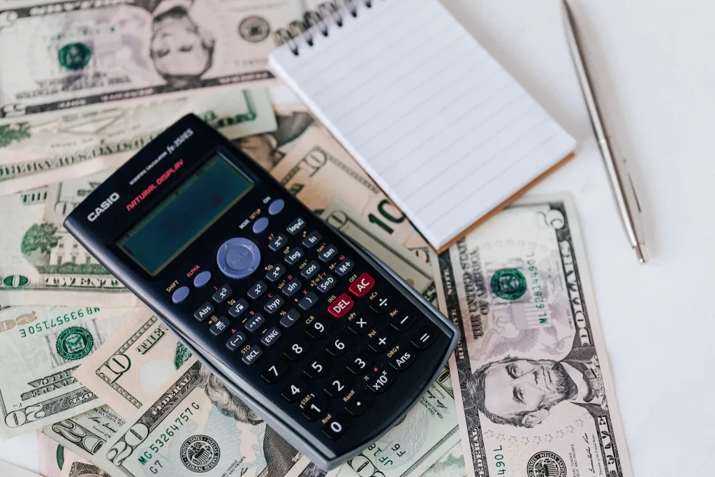 THE 5 BEST WAYS TO FINANCE AN ADU - PLUS ALTERNATIVES TO HELOCS 2 From above electronic calculator and notepad placed over United States dollar bills together with metallic pen for budget planning and calculation