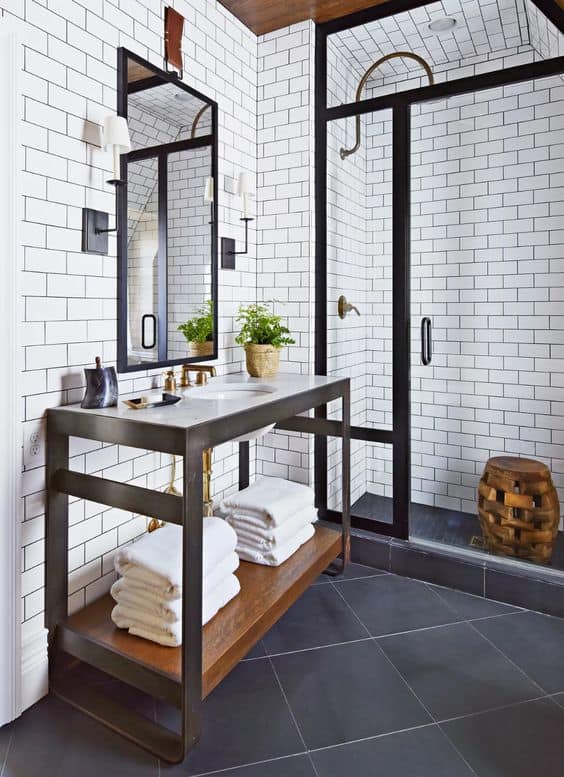 21 STUNNING SHOWER TILE IDEAS FOR SMALL BATHROOMS 1 A subway tiles in a tiny bathroom shower with black accents, gray floor tiles, a wooden vanity with shelves, and brass details.