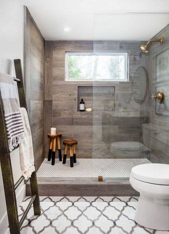 21 STUNNING SHOWER TILE IDEAS FOR SMALL BATHROOMS 4 A tiny bathroom with wood-effect tiling, glass shower, gold accents, and a white geometric-mosaic tiles.