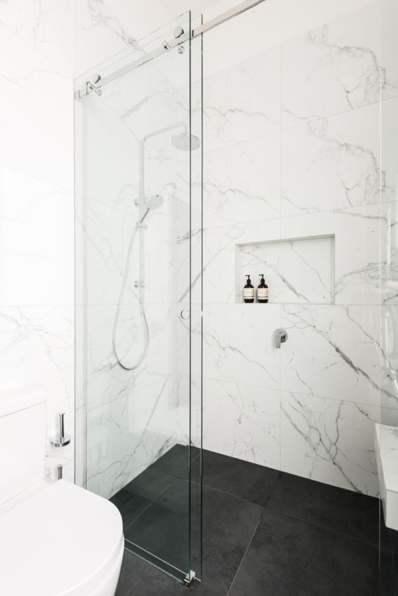 21 STUNNING SHOWER TILE IDEAS FOR SMALL BATHROOMS 12 compact, contemporary bathroom featuring a white toilet, glass shower enclosure, dark marble floor tiles, and marble walls.