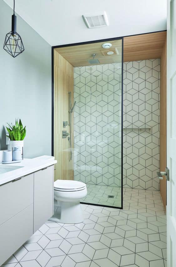 21 STUNNING SHOWER TILE IDEAS FOR SMALL BATHROOMS 19 tiny bathroom including a glass shower with wooden accents, white walls, geometric graphic patterns floor tiles, and a potted plant.