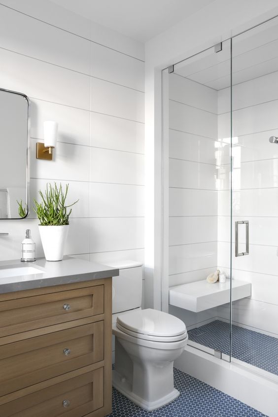 21 STUNNING SHOWER TILE IDEAS FOR SMALL BATHROOMS 18 Small, clean bathroom with a wooden vanity, white tiles, a glass shower partition, blue shiplap floor tiles, and a potted plant.