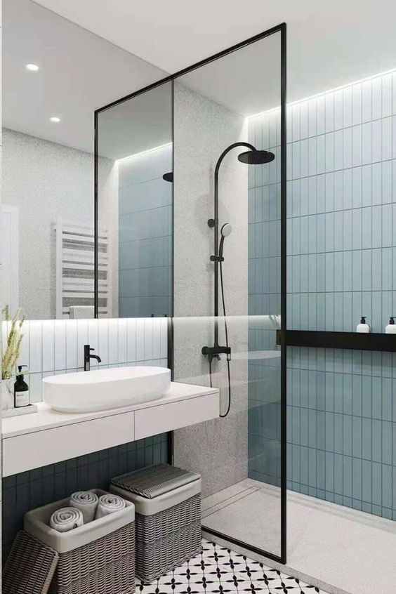 21 STUNNING SHOWER TILE IDEAS FOR SMALL BATHROOMS 15 Sleek bathroom featuring light blue glass tiles, black-framed frameless glass shower enclosure, black shower fixtures, and a floor tile with contrasting patterns.