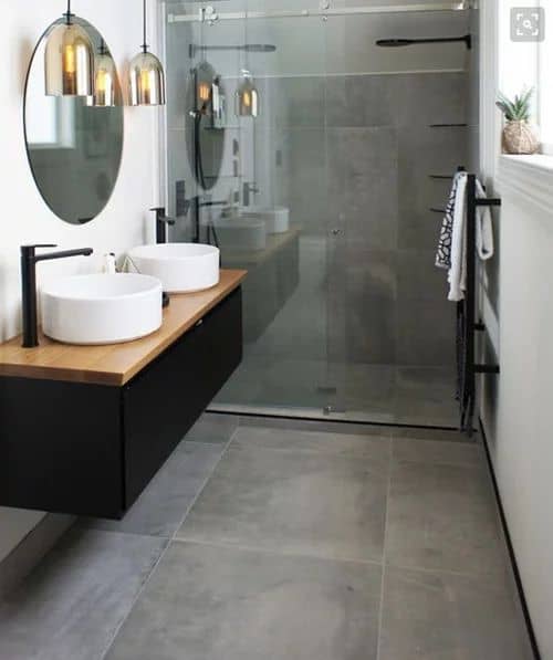21 STUNNING SHOWER TILE IDEAS FOR SMALL BATHROOMS 2 A small bathroom with a wooden vanity, two vessel sinks, round mirrors, pendant lights, and a walk-in shower with large format tiles.