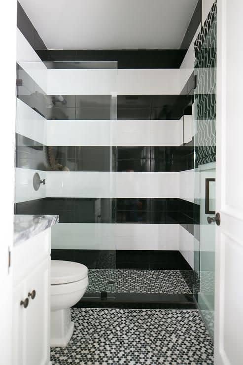 21 STUNNING SHOWER TILE IDEAS FOR SMALL BATHROOMS 10 A sleek, compact bathroom featuring a glass door, geometric black and white tiles, black and white stripes for the shower, and a green accent wall over the toilet.