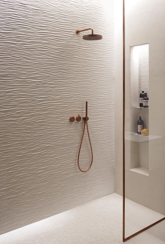 21 STUNNING SHOWER TILE IDEAS FOR SMALL BATHROOMS 16 A small shower space with textured wave-patterned textured tiles, bronze fixtures, and a minimalist glass door.