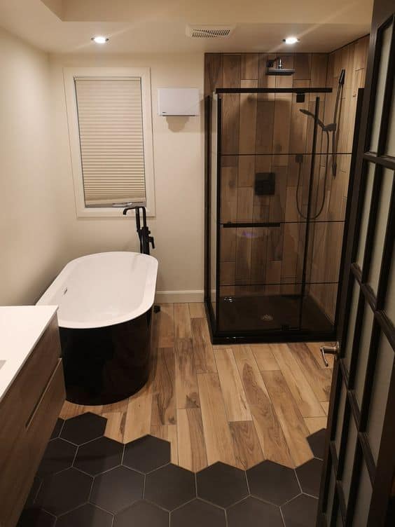 21 STUNNING SHOWER TILE IDEAS FOR SMALL BATHROOMS 3 A small bathroom featuring a corner shower with wooden tiles, a freestanding tub, and contrasting wood-look and dark hexagonal floor tiles.