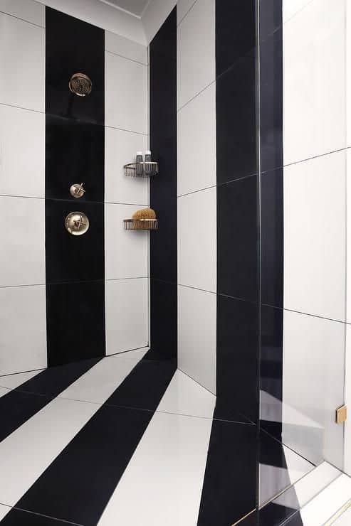 21 STUNNING SHOWER TILE IDEAS FOR SMALL BATHROOMS 7 Sleek shower corner with a striking black and white vertical striped pattern on the wall and floor, gold fixtures, and a built-in shelf for toiletries