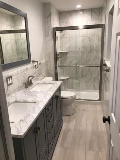 19 SMALL BATHROOM FLOOR TILE IDEAS: ADDING PERSONALITY TO A TINY HOUSE 8 A narrow small bathroom showcasing light wood cabinets, marble countertops, and a spacious glass-enclosed shower with large gray Wood-Look Porcelain Tiles.