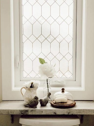 18 SMALL BATHROOM WINDOW IDEAS FOR NATURAL LIGHT AND PRIVACY 10 Cozy bathroom corner with a vintage appeal, featuring a decorative window with diamond-patterned Window Film and a rustic tabletop adorned with a vase.