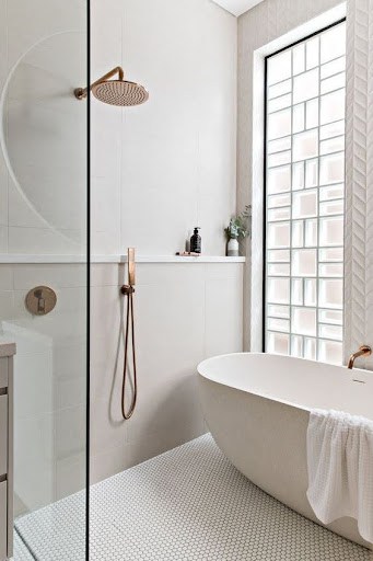 18 SMALL BATHROOM WINDOW IDEAS FOR NATURAL LIGHT AND PRIVACY 12 Sleek bathroom detail showing a white oval tub, herringbone tile wall, and a tall, slim frosted Glass Blocks window providing diffused light and privacy.