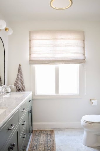 18 SMALL BATHROOM WINDOW IDEAS FOR NATURAL LIGHT AND PRIVACY 13 Chic bathroom with gray vanity, herringbone tile floor, and a compact window dressed with a soft roman shade for a blend of natural light and seclusion."