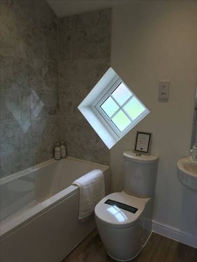 18 SMALL BATHROOM WINDOW IDEAS FOR NATURAL LIGHT AND PRIVACY 21 Skewed perspective of a petite washroom with skewed Corner-Placed Triangle Windows: letting in daylight, above a modern bathtub and adjacent to a pedestal sink.