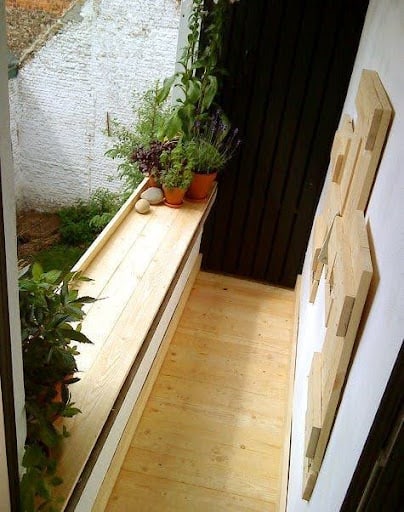 20 SMALL PATIO FURNITURE IDEAS TO MAKE A BIG IMPACT 14 A slender balcony planter box filled with lush greenery Folding Bench, juxtaposed with creative wooden wall accents, exemplifying an efficient use of a small outdoor area.