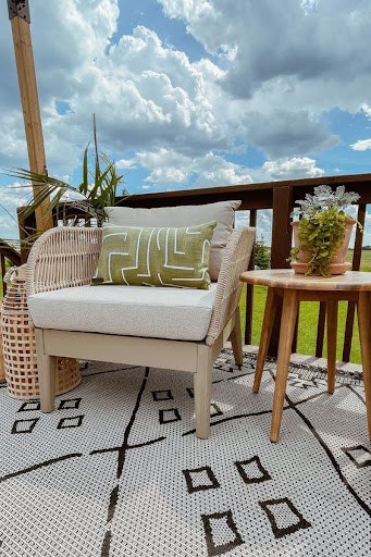 20 SMALL PATIO FURNITURE IDEAS TO MAKE A BIG IMPACT 16 A small outdoor seating arrangement with a wicker armchair and a plush patterned pillow, alongside a wooden side table on a chic rug, ideal for compact deck spaces.