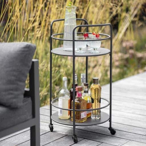 20 SMALL PATIO FURNITURE IDEAS TO MAKE A BIG IMPACT 20 A small mobile bar cart with two tiers, holding an array of drinks and glassware, providing a functional and portable beverage station in a cozy garden corner.