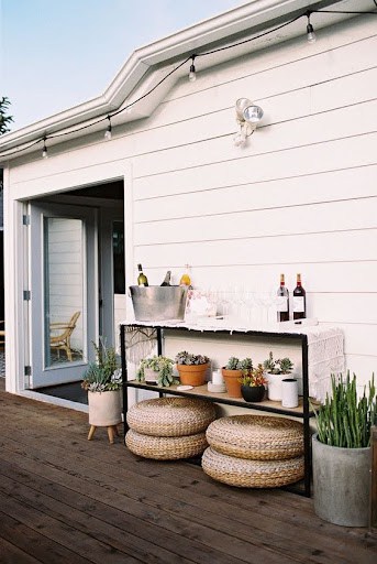 20 SMALL PATIO FURNITURE IDEAS TO MAKE A BIG IMPACT 21 An outdoor serving area with a rustic bar cart, complemented by round woven stools and potted plants, creating a compact entertaining space on a wooden deck.
