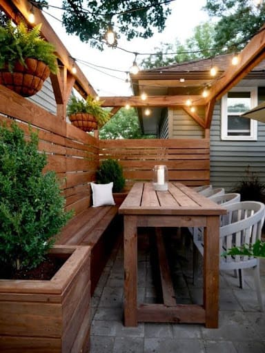 20 SMALL PATIO FURNITURE IDEAS TO MAKE A BIG IMPACT 23 A rustic wooden patio dining area with built-in bench seating under a canopy of twinkling lights, perfect for intimate outdoor gatherings.