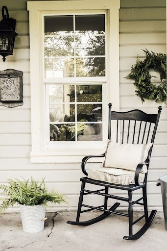 20 SMALL PATIO FURNITURE IDEAS TO MAKE A BIG IMPACT 24 A traditional black rocking chair with a white cushion, placed beside a white window and a vintage post box, adding charm to compact patio decor.