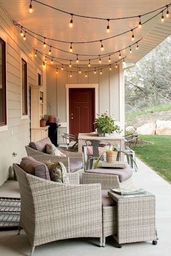 20 SMALL PATIO FURNITURE IDEAS TO MAKE A BIG IMPACT 28 A cozy patio corner with woven chairs and cushions, an inviting red door, and string lights casting a warm glow on small outdoor furniture.