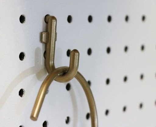 22 AWESOME SMALL WALK-IN CLOSET IDEAS FOR TINY HOMES & ADUS 6 A close-up of a brass hook on a pegboard, exemplifying minimalist and functional design in a small walk in closet