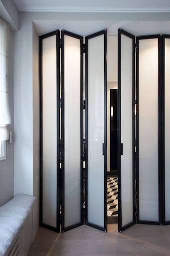 22 AWESOME SMALL WALK-IN CLOSET IDEAS FOR TINY HOMES & ADUS 26 A set of modern black-framed Use of Accordion mirrored doors opening to a sleek wardrobe in a well-lit room.