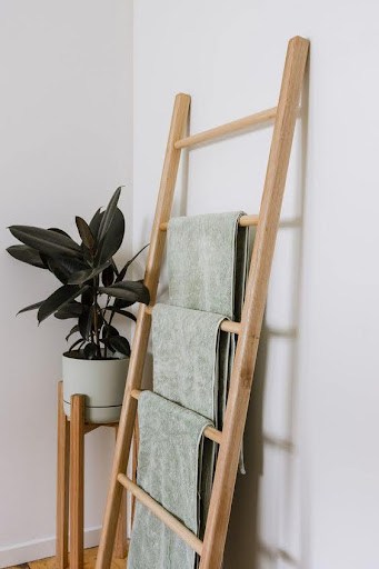 TOWEL STORAGE FOR A SMALL BATHROOM: 19 CREATIVE SOLUTIONS 2 Green towels draped over a wooden ladder, a chic and simple towel storage for small spaces.