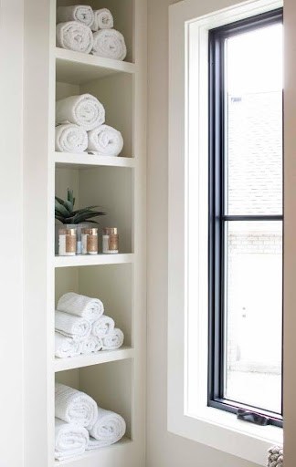 TOWEL STORAGE FOR A SMALL BATHROOM: 19 CREATIVE SOLUTIONS 4 Rolled white towels on narrow shelves next to a window, ideal for a small bathroom's towel storage.