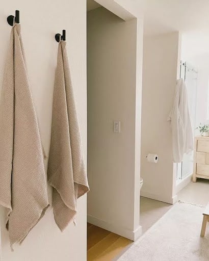 TOWEL STORAGE FOR A SMALL BATHROOM: 19 CREATIVE SOLUTIONS 6 Beige towels hang from black hooks on a white wall, perfect for small bathroom towel storage.