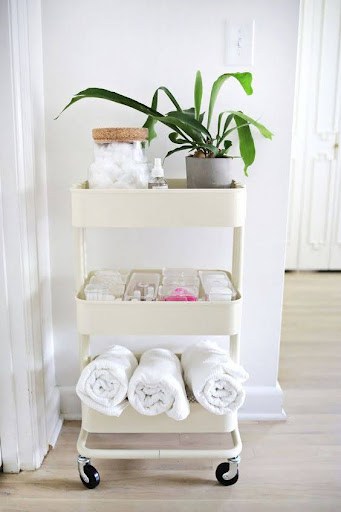TOWEL STORAGE FOR A SMALL BATHROOM: 19 CREATIVE SOLUTIONS 11 A white rolling cart with towels and plants, offering a portable and stylish storage option for small bathrooms.
