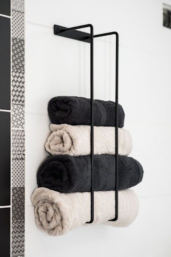 TOWEL STORAGE FOR A SMALL BATHROOM: 19 CREATIVE SOLUTIONS 14 Neatly rolled towels stored in a wall-mounted black metal rack, a modern touch for small bathroom storage.