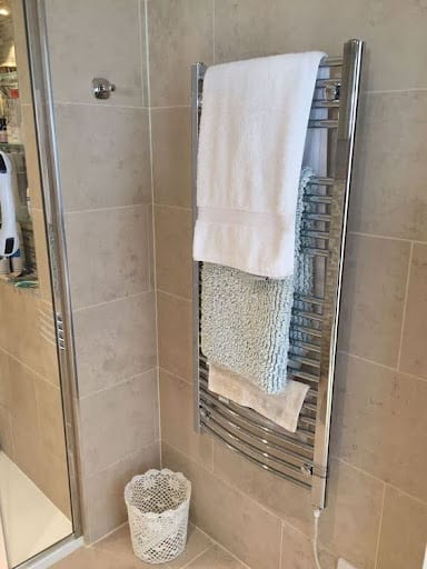 TOWEL STORAGE FOR A SMALL BATHROOM: 19 CREATIVE SOLUTIONS 20 A metal heated towel rail with a basket underneath, providing warm towels and extra storage in a small bathroom.