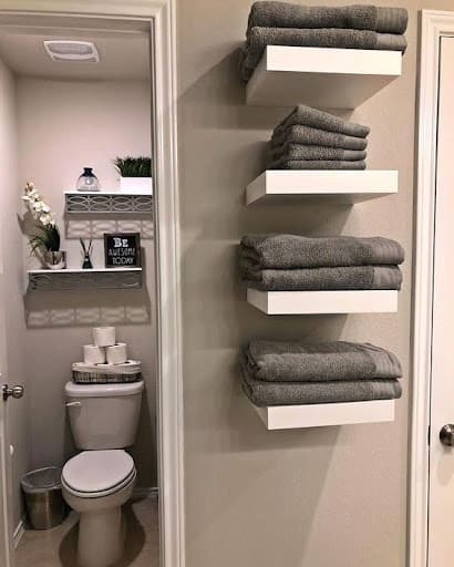 TOWEL STORAGE FOR A SMALL BATHROOM: 19 CREATIVE SOLUTIONS 23 Gray towels neatly folded on floating Vertical Towel Storage Cabinet: against a textured wall, offering a streamlined look for small bathroom towel storage.