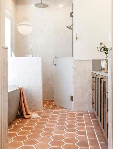 19 SMALL BATHROOM FLOOR TILE IDEAS: ADDING PERSONALITY TO A TINY HOUSE 22 A cozy powder room features terracotta hexagon floor tiles and a glass-walled shower, enhancing the intimate space with warm tones and clean lines.