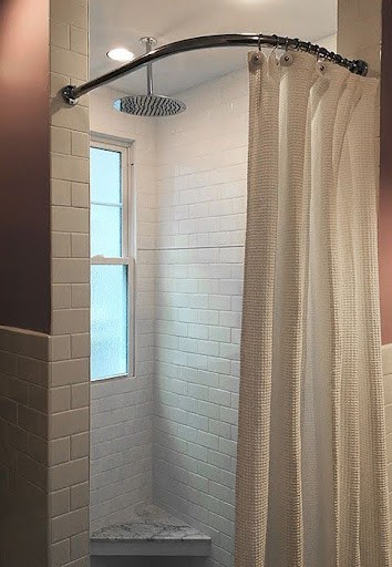 21 SMALL BATHROOM SHOWER IDEAS PERFECT FOR TINY HOUSES & ADUS 6 A small bathroom shower with a curved shower rod and beige curtain partially drawn, showcasing a window.