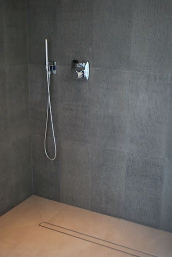 21 SMALL BATHROOM SHOWER IDEAS PERFECT FOR TINY HOUSES & ADUS 10 Small shower area with a Linear Drain and simple hand-held shower fixture against a dark tiled wall, showcasing understated design.