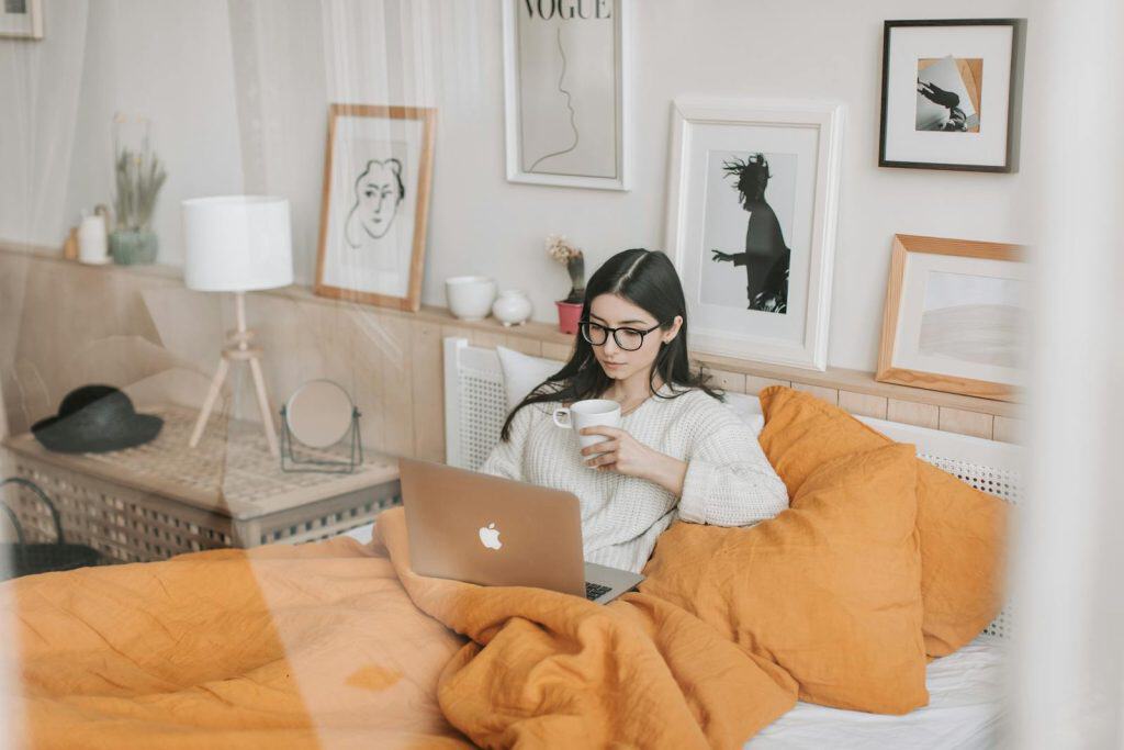 DIFFERENCES BETWEEN A TOWNHOUSE AND A CONDO: SIMPLIFIED & EXPLAINED 5 Focused young brunette in eyeglasses with cup of hot drink lying in comfortable bed and working on laptop in morning